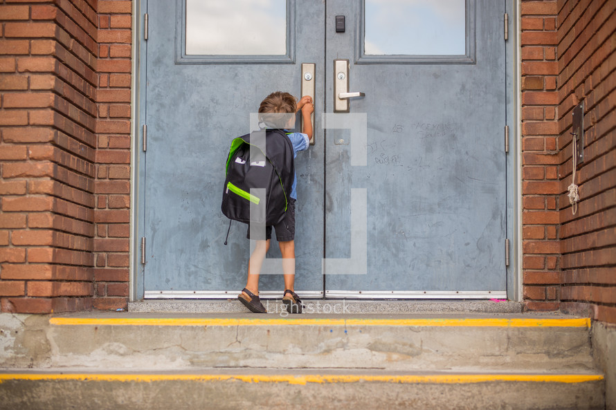 a boy with a backpack standing in front of school doors 