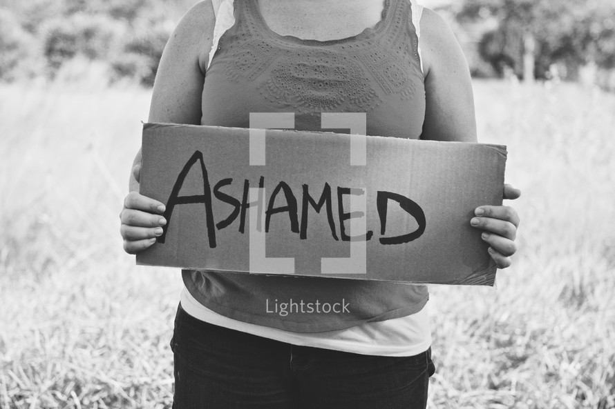 woman holding a sign that reads ASHAMED