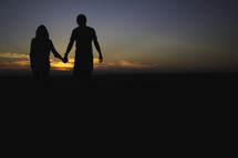 Silhouette of a man and woman holding hands before a sunset.