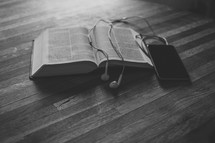 smartphone, earbuds, and an opened Bible 