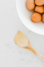 brown eggs in a white bowl and wooden spoon 