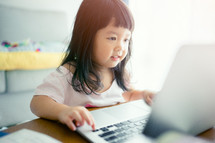 Little Asian girl with laptop computer or notebook in living rome at home.