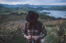 a man in a hat and plaid shirt standing on a mountain top 