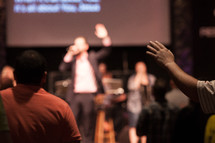 a preacher giving a sermon and raised hands at a worship service 