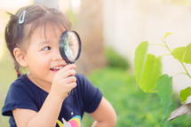 child looking at leaves through a magnifying glass 