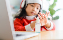 a little girl in a Santa suit using spray-on hand sanitizer 