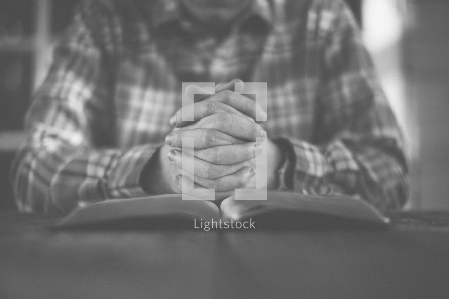 A man with hands folded in prayer on an open Bible