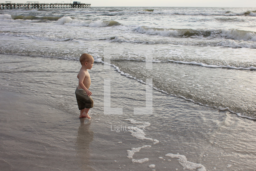 A little boy wades in the ocean.