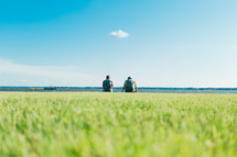 Two men sitting by a lake next to each other with a grassy foreground