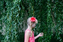 A little blonde girl walks along a wall with hanging green vines.