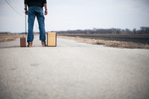 man looking down a road standing next to suitcases