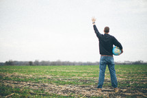 man holding a globe standing in a field with his hand raised in worship