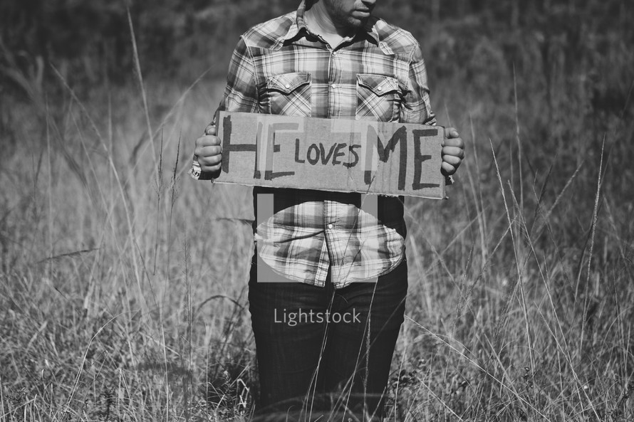 Man holding "He Loves Me" cardboard sign