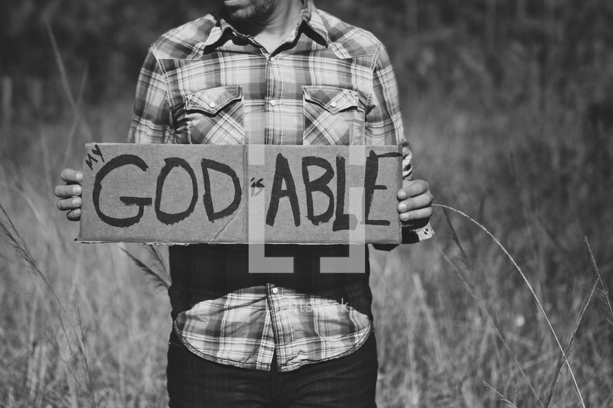 man holding a sign with the words God is able