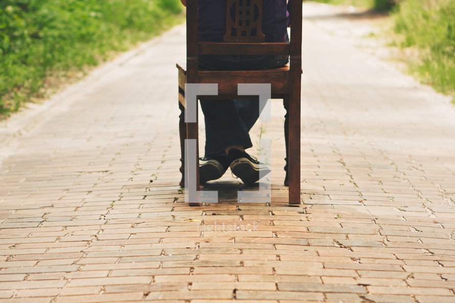 A person sitting on a chair on a brick sidewalk.