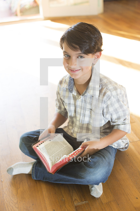 A boy sitting on the floor and reading the Bible.