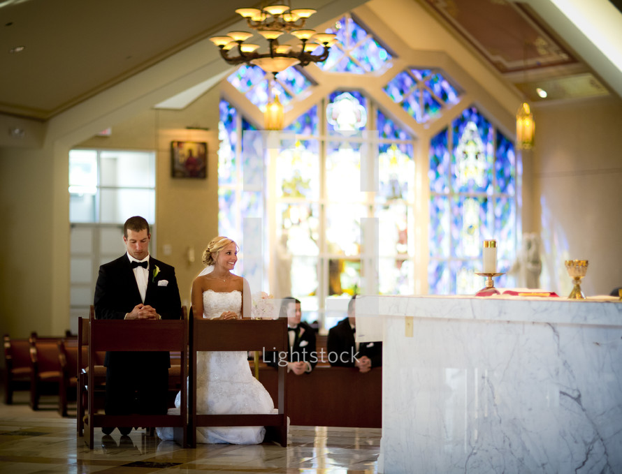 bride and groom kneeling in prayer at an altar during rehearsal 