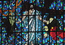 A stained glass window depicting scenes from the life of Christ including Jesus after He was resurrected from the dead, a rooster that crowed three times before Peter denied Jesus, wheat grain and other biblical symbols from the New Testament story of Jesus including the old rugged cross and the crown of thorns that the Roman soldiers pressed on Jesus head. 