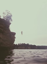 man jumping off a cliff into the water 