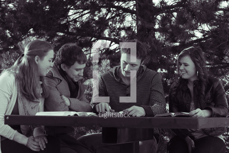 college students reading their Bibles outdoors at a picnic table during a Bible study