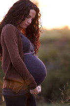 Pregnant woman standing outside at sunset.