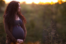Pregnant woman standing outside at sunset.