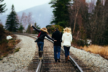 Three people walk along a railroad track.