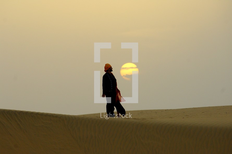 man standing in front of the setting sun in the desert 