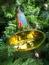 A brass Christmas bell decoration hanging on a Christmas tree reflecting the colors and glory of the Christmas season.
