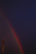  A communications tower is juxtaposed with a rainbow on a dark sky.