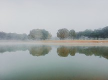 reflection of trees on pond water and morning fog 