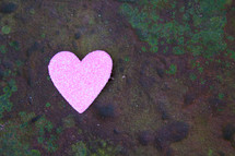 A single pink heart on a rock covered in green moss.