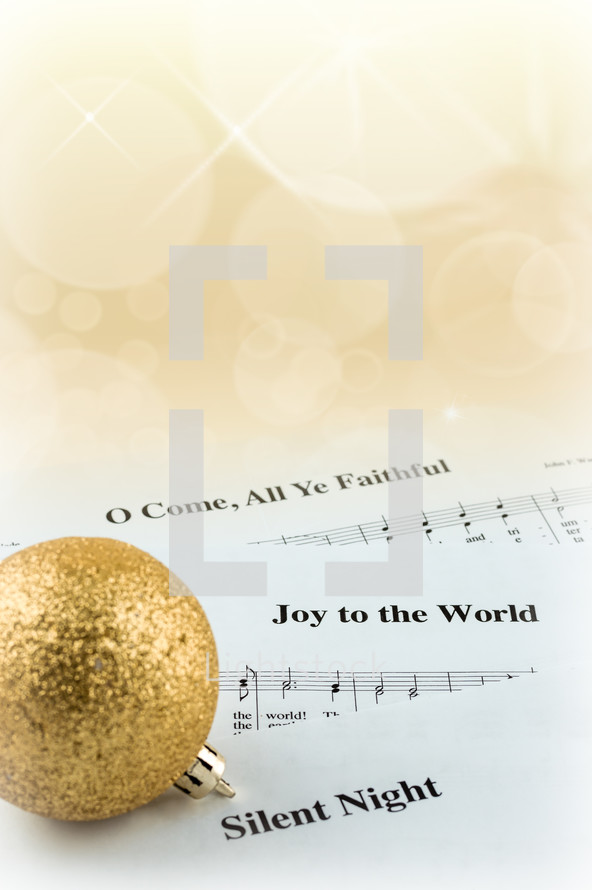 A gold Christmas ball on pages of sheet music of Christmas carols.