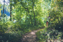 woman walking on a trail leading to a lake 