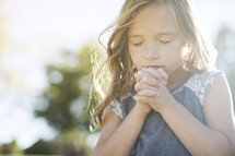 Little girl in prayer outside with sun shining.