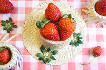 Fresh strawberries decorated on a straw hat. on a red picnic blanket.