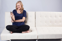 woman texting on a white couch 