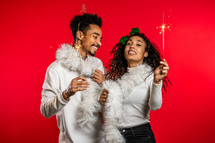 Young african american couple with christmas bengal fire sparklers isolated on red background studio. New 2025 year decorations, party, happiness concept. High quality photo

