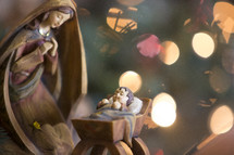 A nativity sculpture lit by Christmas tree lights.