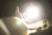 a hand reaching towards glowing light 