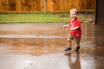 a toddler boy splashing in a puddle 