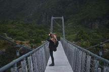 woman on a swinging bridge taking a picture with a camera 