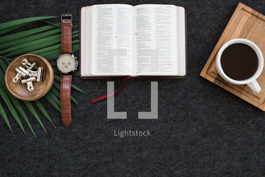 watch, Bible, coffee, tray, and palm fronds on a desk 