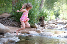a girl child jumping into a stream in her swim suit 