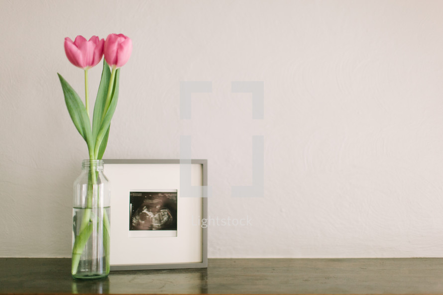 A vase with pink tulips next to a framed photo.