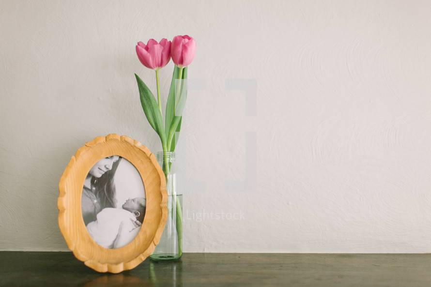 A vase of pink tulips next to a framed photo of a mother and newborn baby.