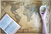 woman reaching for a mug with a Bible on a world map 