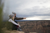 happy couple sitting on a mountaintop looking out. 