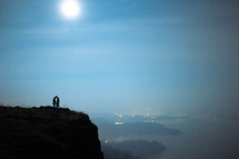 silhouette of a couple standing at the edge of a cliff at night 