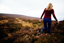 a young woman walking through a field of tall brown grasses 